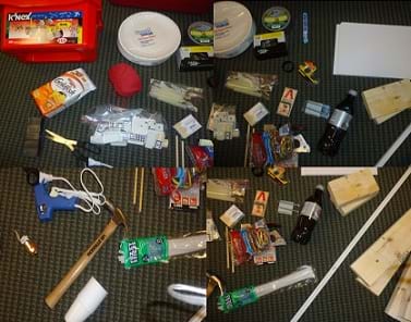 Four photos show a range of materials and tools lying on the floor: red box of K'NEX components, paper plates, goldfish crackers, yarn, glue gun and glue sticks, nails, duct tape, candies, scotch tape, paper, boards, corner edging, soda pop, mouse traps, toothpicks, staple gun, staples, dominoes, scissors, magnets, pipe cleaners, hammer, pulley, toy car, cups, screws, small dowels, rubber bands and marbles.