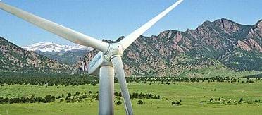 Photo shows a three-bladed wind turbine with a backdrop of mountains.