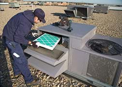 A photograph shows a technician inspecting the filter on a rooftop air conditioning unit.