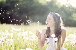 A girl blowing a dandelion in the grass.