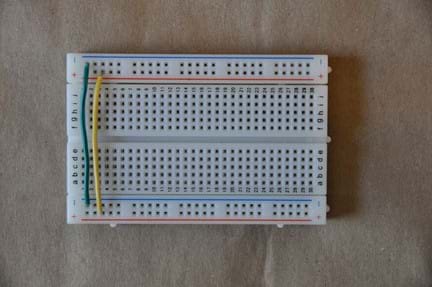 Photo shows a breadboard (circuit board) with a yellow wire, which connects the positive terminals on either side of the board, and a green wire, which connects the negative terminals on either side of the board.
