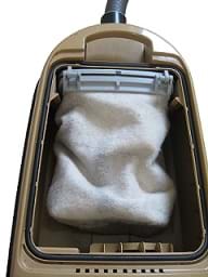 A photograph shows the back of an upright vacuum cleaner with the plastic cover removed so that the soft, fabric cleaner bag is shown.