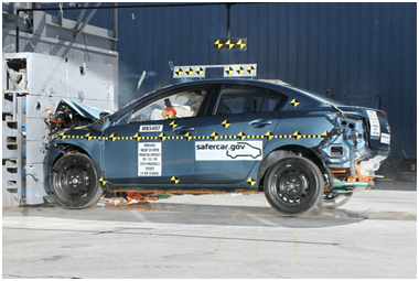 A photograph shows a sedan automobile after an indoor crash test with its front end crumpled where it hit a wall head on.
