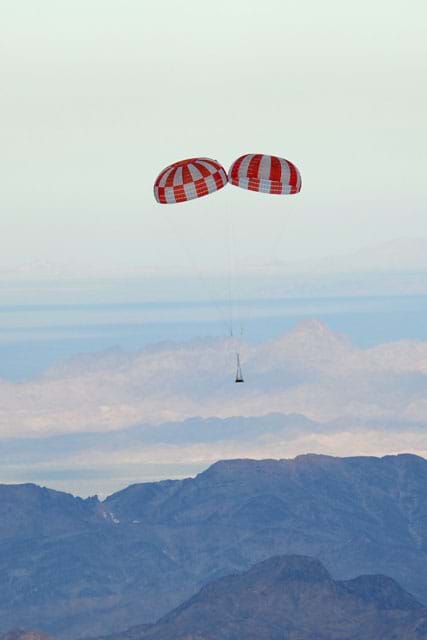 A photograph shows a NASA robot floating to the ground, slowed by a double parachute.