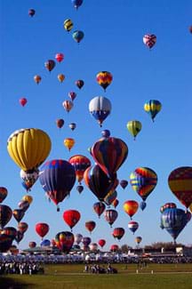 Photo shows more than 50 colorful hot air balloons rising from a field into the blue sky.