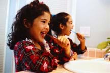 Photo shows two young girls brushing their teeth over a sink.