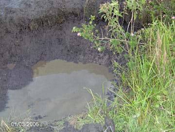 Photo shows a hole in the ground filled with dirty, still water.