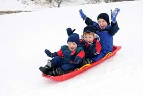 Three young boys on a sled playing in the snow.