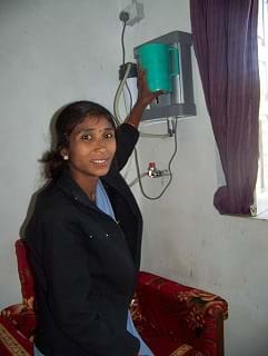A photo shows a female health aide using a water filter mounted to the wall in a room.
