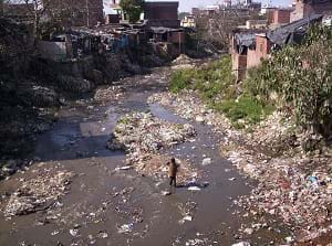A polluted rubbish-laden river surrounded by slum shacks and trash in the Indian Himalayas.