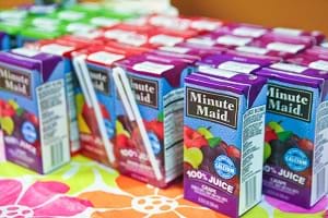 A photograph shows ~20 single-serving rectangular Minute Maid juice boxes with attached straws on a table top.