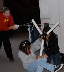 A photograph shows three students launching a t-shirt from a big y-shaped device made of PVC piping; it looks like a big slingshot.
