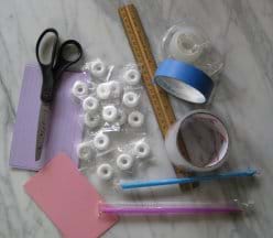 A photo shows scissors, tape, ruler, straws, lifesaver-shaped white candies and index cards in a pile on a tabletop.