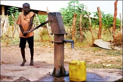 A boy pushes down on a lever as he pumps water into a yellow container.