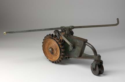 Photo shows a steel garden sprinkler shaped like a tractor with one small front wheel and two larger, treaded back wheels.