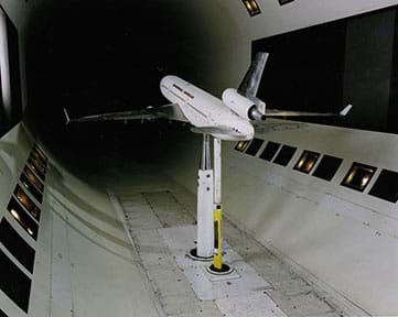 A photograph shows a small-sized a passenger airplane mounted from below inside a wind tunnel.