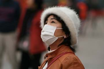 A photograph shows a woman wearing a white cloth mask over her moutn and nose to protect against air pollution in China.