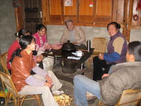 Photo shows six adults sitting around a coal stove inside a home.