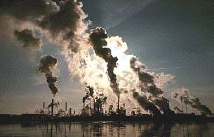 A photograph of a factory releasing air pollutants near a body of water.