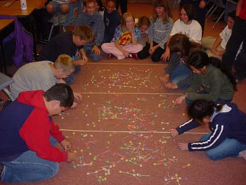 Students cluster around a carpeted area strewn with molecules made from toothpicks and gumdrops.
