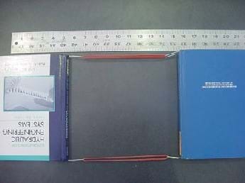 A photo shows two books attached together with a sling-type setup made with rubber bands and paperclips. A ruler is in place to measure the movement of the books before and after the books are pulled apart.  