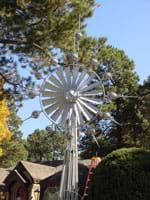 Photo shows a silver windmill-type outdoor kinetic sculpture.