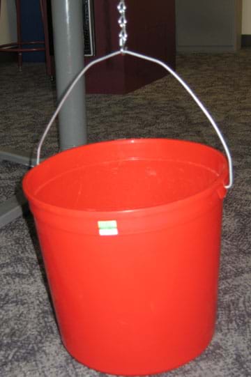 Photo shows the handle of a red bucket held up by an S-hook and chain.