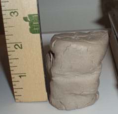 Photo shows a clay column next to a ruler, measuring its reduced 2-inch height after carrying a load of books.