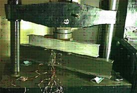 Photo shows an I-beam section in a metal machine applying a large compressive force.