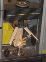 Photo shows a balsa wood structure crushed and splintered inside a glass box.