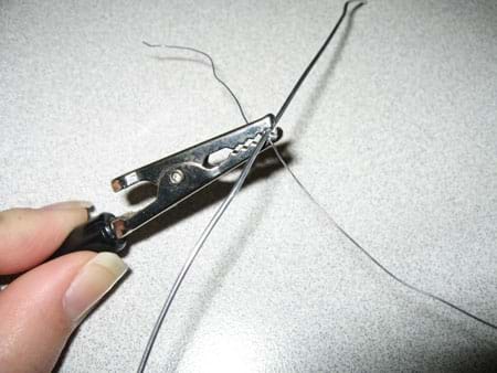 Photo of an alligator clip clasping two wires together.