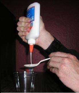 Photo shows hands sqeezing white glue from a bottle onto a plastic spoon.