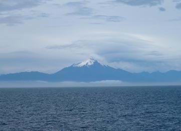 A photograph shows a vast sea in the foreground with a pointed, snow-capped, blue-tinted mountain on the distant shore.