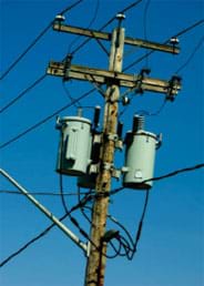 A photograph of a telephone pole, showing the top half of the pole with the connecting and draping wires and green glass insulators against a background of a blue sky.