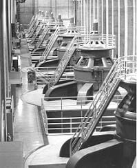 A black and white photo shows a row of huge steel turbines with ladders.