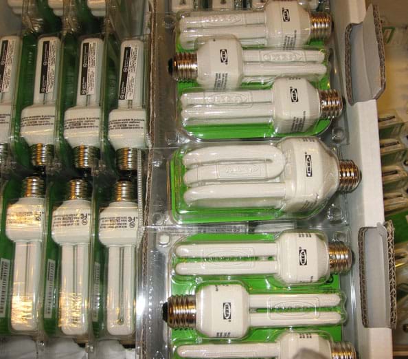 Photo shows a bin of packaged light bulbs for sale in a store.