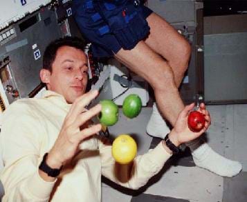 Photo shows an astronaut attempting to hold onto apples while in space. The apples are floating around him.