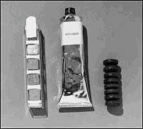 Photo shows three items. The tube looks like a toothpaste tube, and one of the snacks looks like a small stack of eight mini-car tires. The other snack appears to be a set of small cubes placed in a metal holder. 