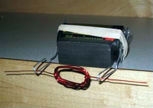 A photo shows a magnet and battery together, with the rubber band holding the bent paperclips in place, all perched on a table edge. The wire coil rests across the paperclip cradles, which extend beyond the table edge.