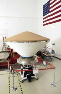 The aeroshell in a NASA lab. The brown colored heat shield is on top while the white backshell is on the bottom.