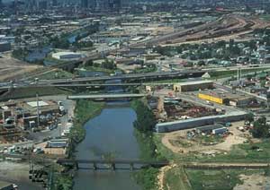 Aerial photo shows a river flowing through an urban area with bridges, highways, warehouses and homes.