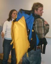 Photo shows a young man wearing a blue backpack with a yellow, pillow-shape sticking out from it.