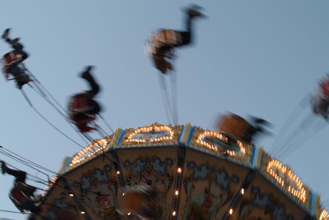 A photo shows seated people swinging and spinning from an amusement park ride that moves in a circle.