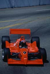 Photo shows a red race car on an asphalt track.