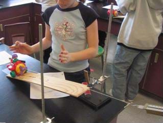 A photograph of a student at lab table watching a toy airplane being pulled up inclined plane.