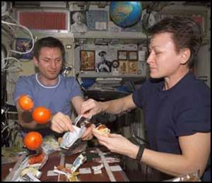 Photo shows a man and a woman holding food and using utensils as three oranges float nearby.