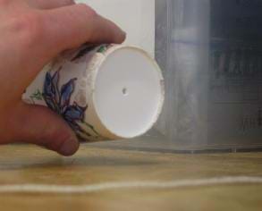 Photo shows a hand holding a paper cup tipped sideways showing a hole in its bottom.