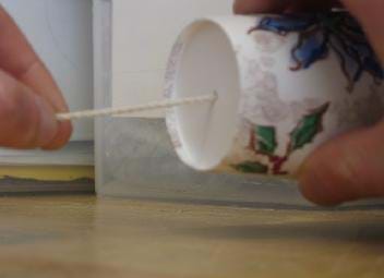 Photo shows one hand holding a paper cup sideways with a string coming out of the bottom and fingers of another hand pulling the string tail taut and away from the cup. 