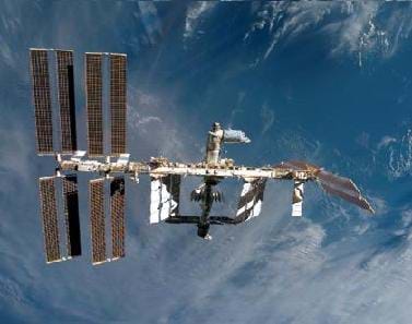 Photo shows the Earth's blue, cloudy atmosphere behind a leggy, floating structure with solar panels.