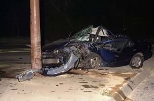 A car crashing into a telephone pole, showing the front end of the car crumpled.